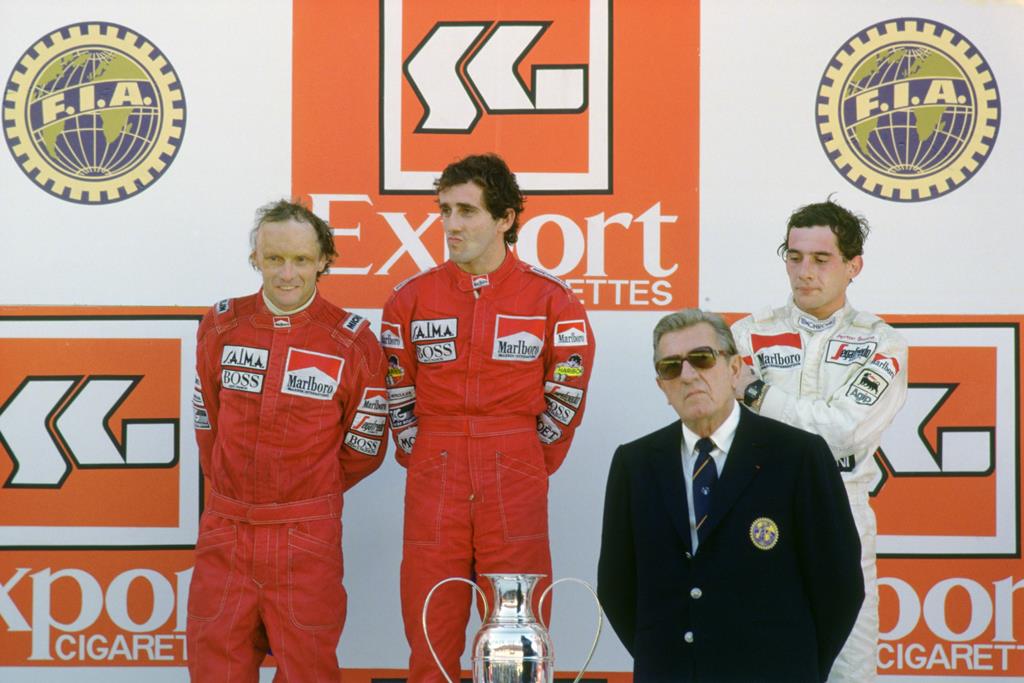 No pódio, Lauda consolou um Alain Prost emocionado. No ano seguinte, Prost não daria sequer hipóteses ao austríaco. Foto: Action Images / Sporting Pictures / Crispin Thruston No pódio, Lauda consolou um Alain Prost emocionado. No ano seguinte, Prost não daria sequer hipóteses ao austríaco. Foto: Action Images / Sporting Pictures / Crispin Thruston