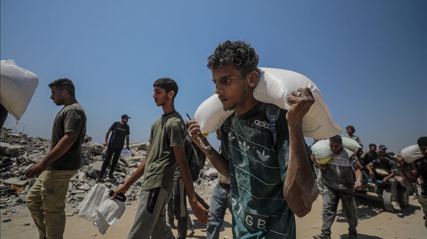 Jovem palestiniano carrega saco com farinha junto ao centro de distribuição de Zikim, no norte de Gaza, durante pausa tática na guerra. Foto: Mohammed Saber/EPA