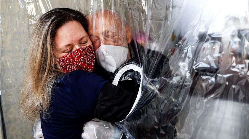 Uma filha abraça o pai através de uma cortina de plástico durante a pandemia, em São Paulo. Foto: Sebastião Moreira/EPA