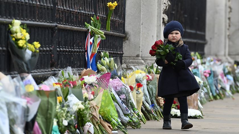 Uma criança deposita flores junto ao Buckingham Palace, após a morte do príncipe Filipe, marido da rainha Isabel II. Foto: Andy Rain/ EPA